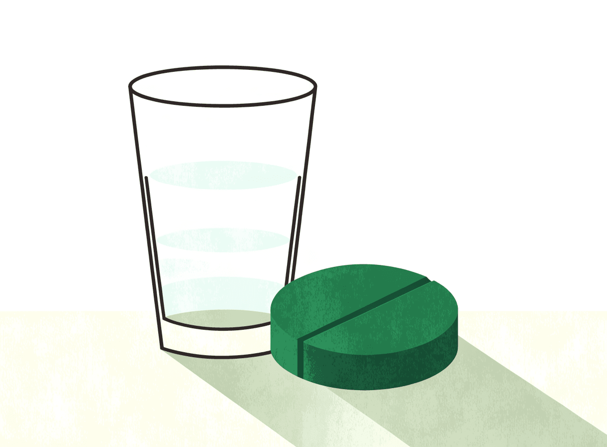 Una tableta redonda junto a un vaso de agua
